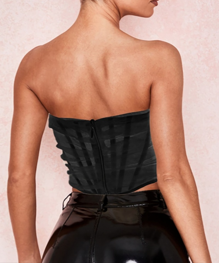 Modelo feminina vestindo corset estruturado com camadas de tule translúcido e acabamento drapeado em diagonal. Modelagem tomara que caia com recorte em V na barra. Estética moderna e elegante, ideal para composições ousadas e sofisticadas.