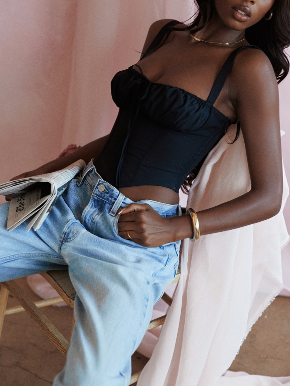 Corset preto com estrutura modeladora, recortes verticais e busto franzido com laço central. Alças largas e fechamento lateral. Modelo feminina vestindo a peça contra fundo neutro, foco do busto à cintura.