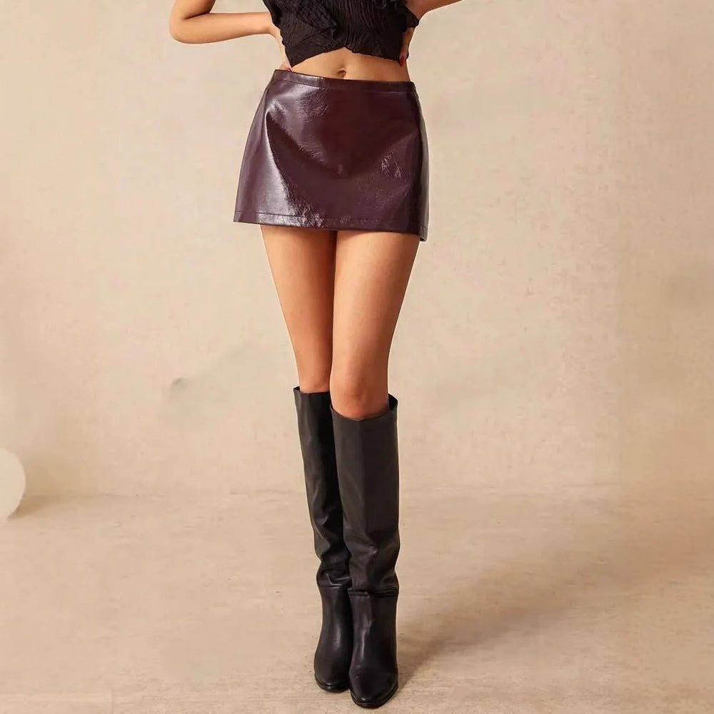 Modelo feminina usando saia de couro com modelagem reta e justa, comprimento mini, acabamento brilhoso e detalhe de cinto discreto na cintura. A peça valoriza o quadril e tem estética urbana, sexy e sofisticada.