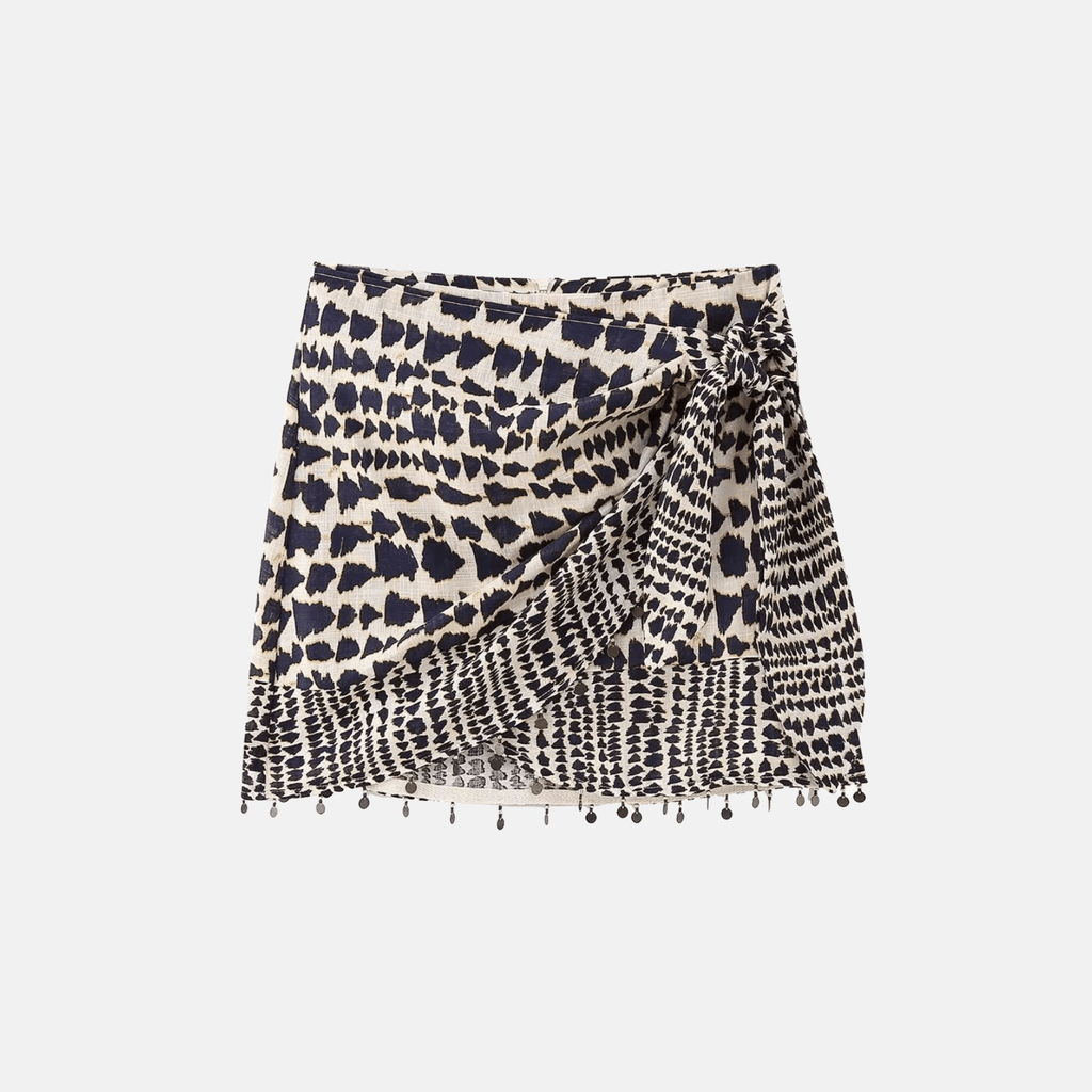 Saia feminina transpassada com estampa tribal, amarração frontal ajustável e aplicação de pompons na barra. Caimento leve, tecido fluido e cintura baixa, ideal para composições tropicais, boho chic ou looks de verão com atitude.