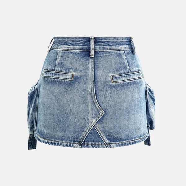 Modelo feminina vestindo saia jeans mini com bolsos cargo laterais volumosos, detalhes em zíper e amarração. A peça possui lavagem azul estonada e recortes assimétricos, com estilo urbano, ajustado e visual utilitário moderno.

