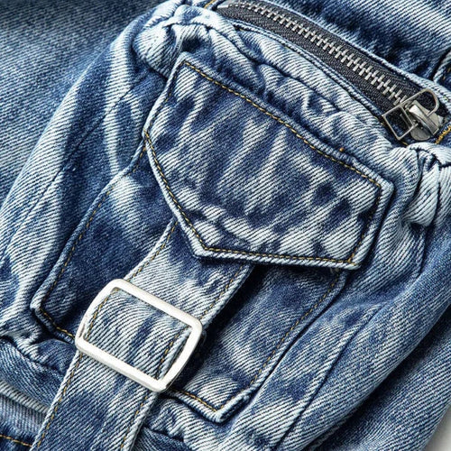 Modelo feminina vestindo saia jeans mini com bolsos cargo laterais volumosos, detalhes em zíper e amarração. A peça possui lavagem azul estonada e recortes assimétricos, com estilo urbano, ajustado e visual utilitário moderno.


