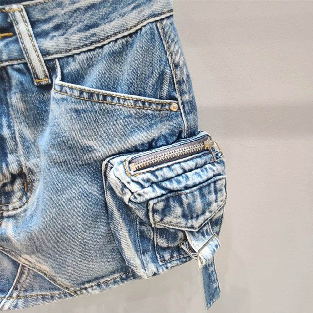Modelo feminina vestindo saia jeans mini com bolsos cargo laterais volumosos, detalhes em zíper e amarração. A peça possui lavagem azul estonada e recortes assimétricos, com estilo urbano, ajustado e visual utilitário moderno.

