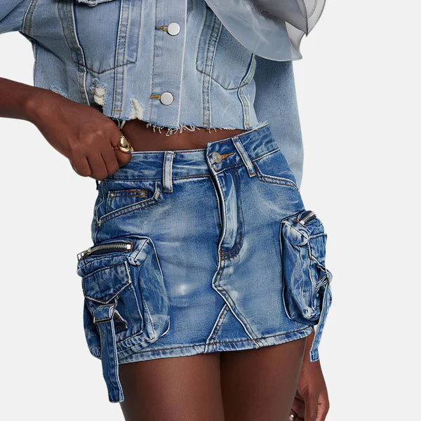Modelo feminina vestindo saia jeans mini com bolsos cargo laterais volumosos, detalhes em zíper e amarração. A peça possui lavagem azul estonada e recortes assimétricos, com estilo urbano, ajustado e visual utilitário moderno.

